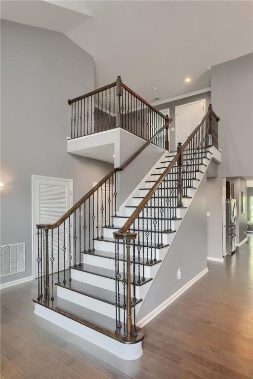 staircase featuring baseboards, wood finished floors, a high ceiling, and recessed lighting