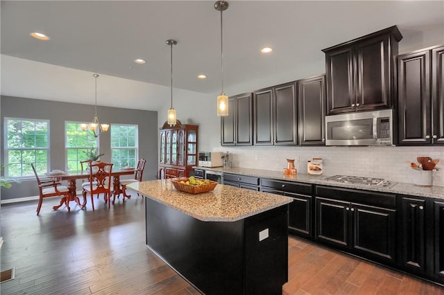 kitchen with appliances with stainless steel finishes, backsplash, light stone countertops, wood finished floors, and a center island