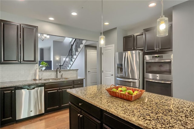 kitchen featuring stainless steel appliances, a sink, light wood-style flooring, decorative backsplash, and light stone counters