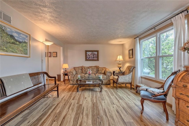 living area featuring a textured ceiling, light wood-style flooring, and baseboards