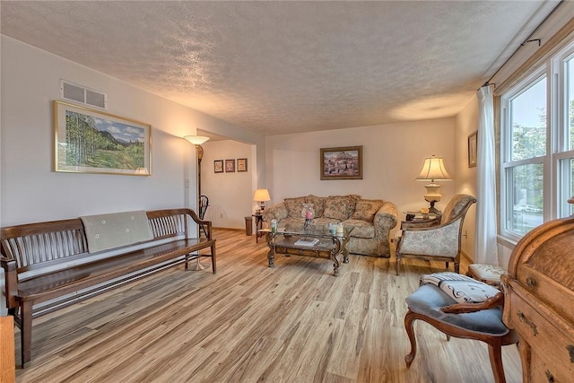 living room featuring a textured ceiling, light wood-style floors, and baseboards