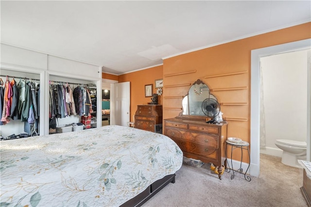 bedroom featuring multiple closets, carpet floors, crown molding, baseboards, and ensuite bath