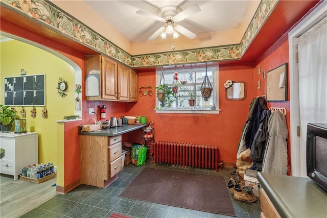 kitchen featuring radiator heating unit, a ceiling fan, brown cabinets, and dark countertops
