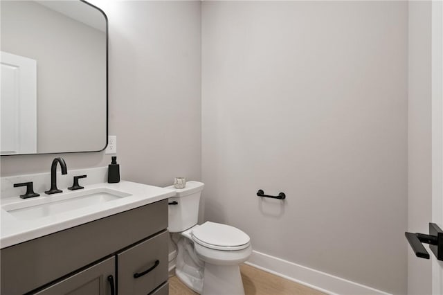 half bath with toilet, vanity, baseboards, and wood finished floors