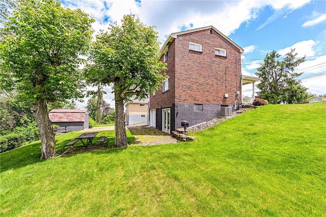 back of house featuring brick siding, a yard, and central AC