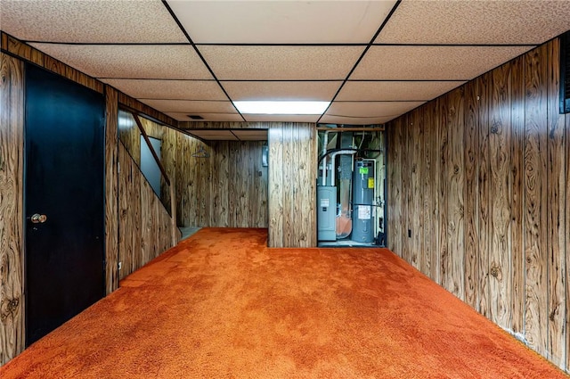 finished below grade area with wood walls, a paneled ceiling, water heater, carpet flooring, and stairs