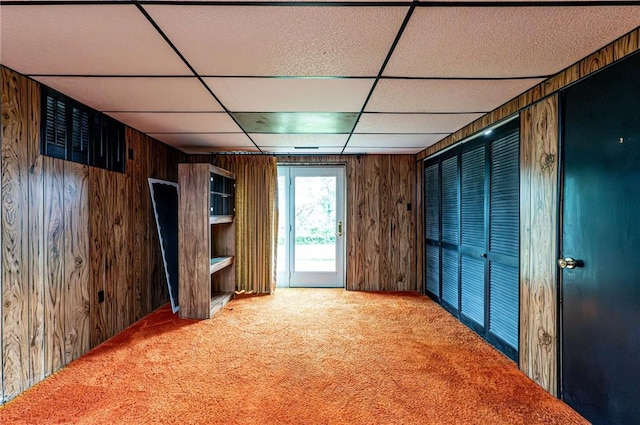 spare room with carpet, a drop ceiling, and wood walls