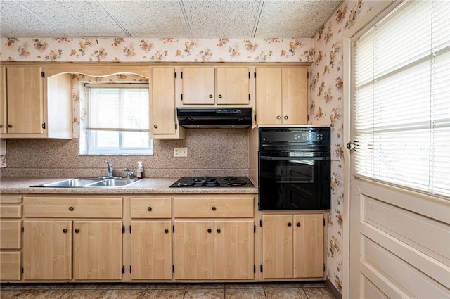 kitchen with black appliances, wallpapered walls, under cabinet range hood, light brown cabinetry, and a sink