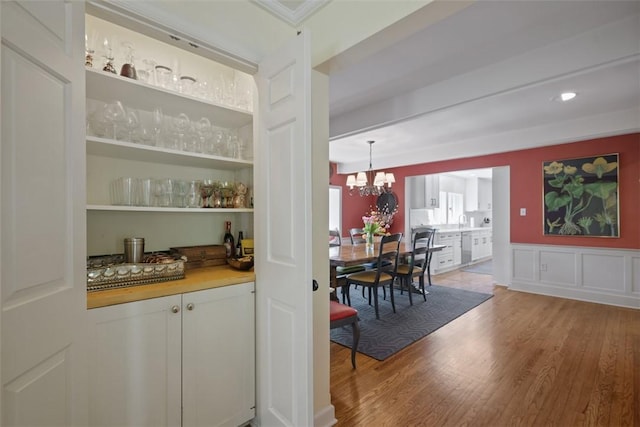 bar area with wood finished floors, wainscoting, a chandelier, stainless steel dishwasher, and a sink