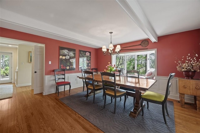 dining area featuring a chandelier, beam ceiling, light wood-type flooring, a wainscoted wall, and a decorative wall