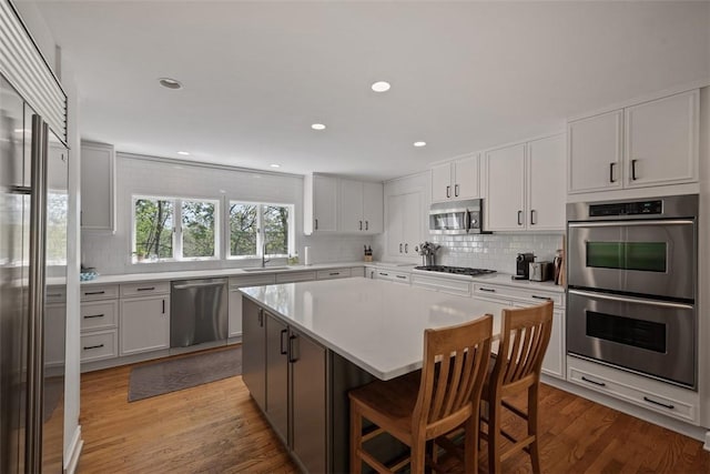kitchen with stainless steel appliances, a sink, backsplash, light countertops, and light wood-style floors