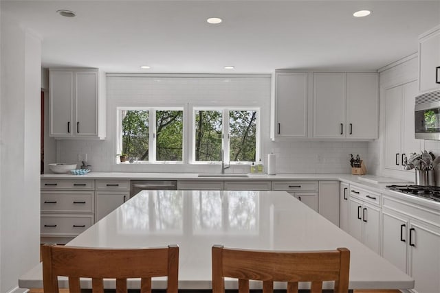 kitchen with a sink, stainless steel appliances, decorative backsplash, light countertops, and recessed lighting