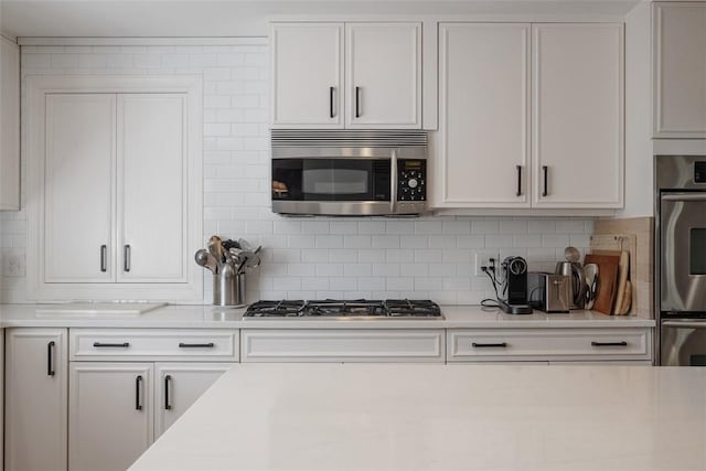 kitchen with appliances with stainless steel finishes, light countertops, decorative backsplash, and white cabinets
