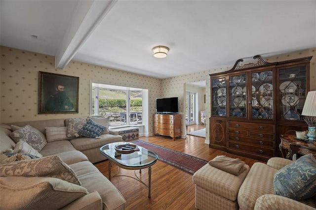 living area with wallpapered walls, wood finished floors, and beamed ceiling