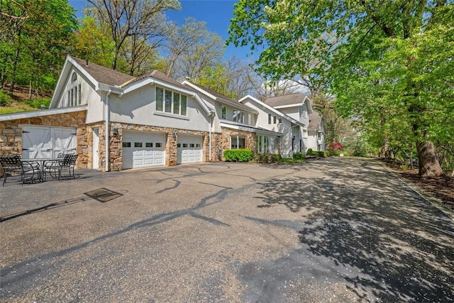 view of front facade with stone siding, stucco siding, asphalt driveway, and a garage