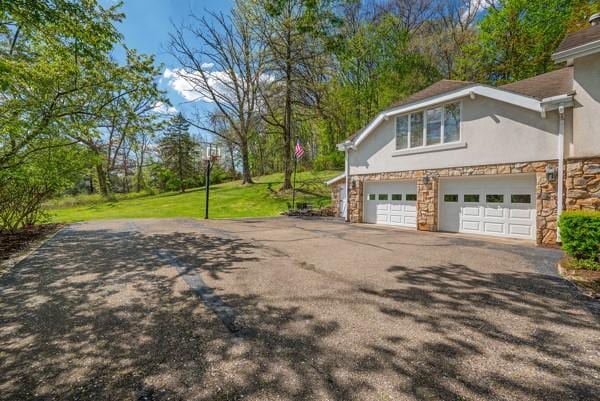 view of side of home with asphalt driveway, stone siding, stucco siding, a garage, and a yard
