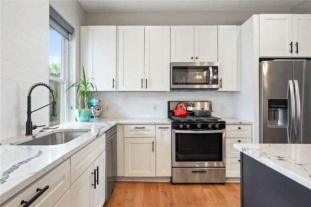 kitchen with appliances with stainless steel finishes, a sink, white cabinetry, and backsplash