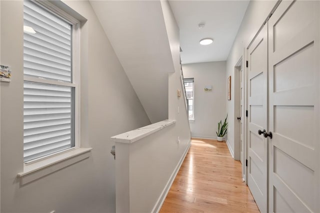 hall with light wood finished floors, baseboards, and an upstairs landing