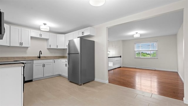 kitchen with appliances with stainless steel finishes, a sink, white cabinetry, light countertops, and a baseboard heating unit