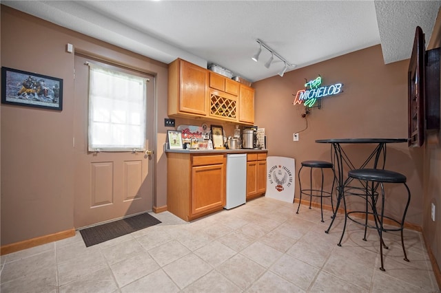 kitchen featuring a textured ceiling, light tile patterned floors, baseboards, and rail lighting