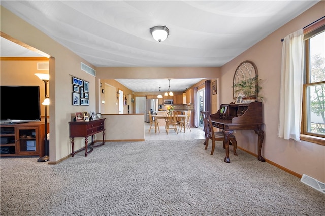 living area with light carpet, healthy amount of natural light, a chandelier, and baseboards