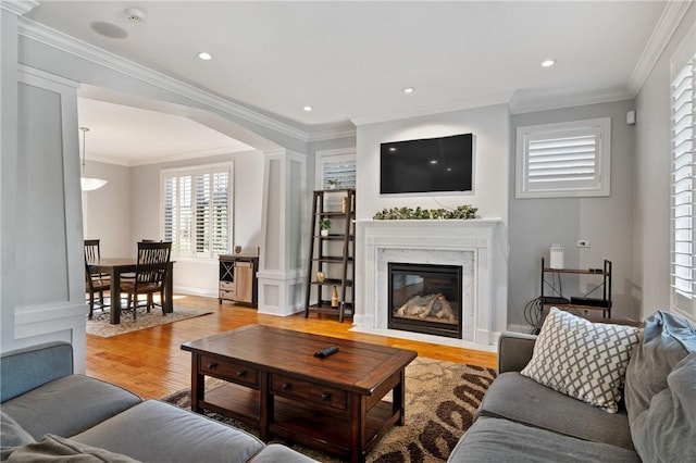 living room with light wood-style floors, crown molding, arched walkways, a fireplace, and decorative columns