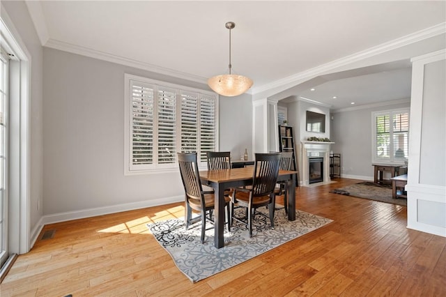dining area featuring light wood finished floors, a fireplace with flush hearth, crown molding, baseboards, and recessed lighting