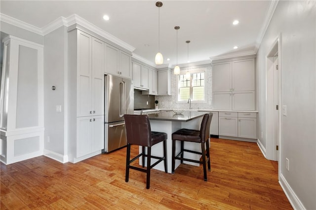 kitchen with high end refrigerator, a breakfast bar area, light wood finished floors, a center island, and ornamental molding
