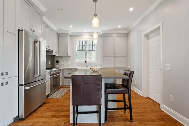 kitchen featuring high quality appliances, ornamental molding, tasteful backsplash, light wood-style floors, and baseboards