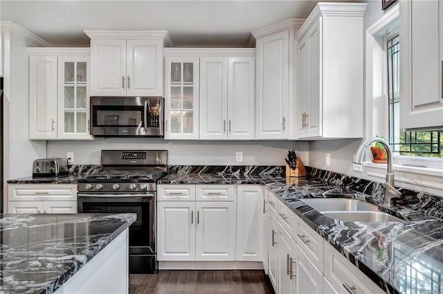 kitchen with appliances with stainless steel finishes, a sink, white cabinets, and dark wood-type flooring