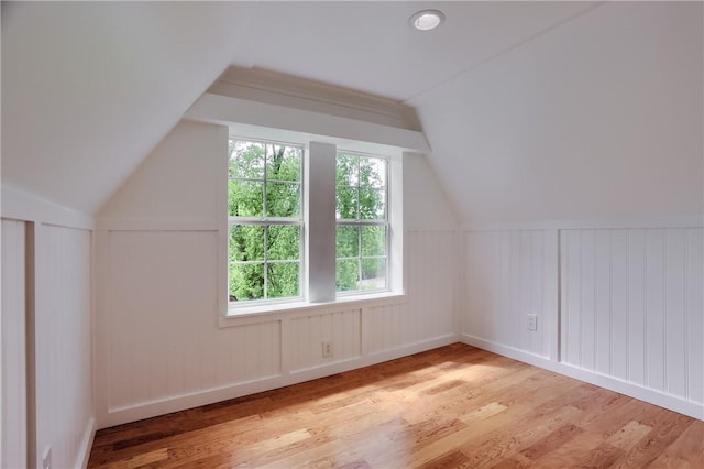 additional living space with a decorative wall, wood finished floors, and lofted ceiling