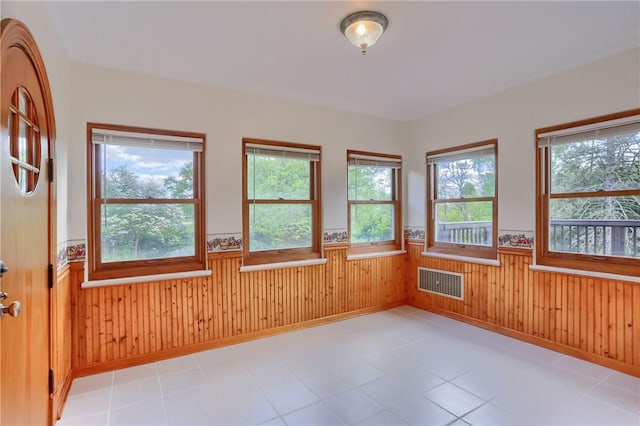 unfurnished room featuring a wainscoted wall, wood walls, and light tile patterned floors