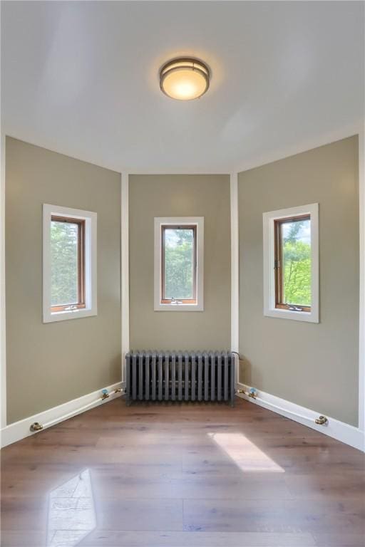 empty room with radiator, baseboards, and wood finished floors