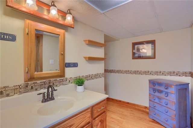 bathroom with wood finished floors, vanity, a drop ceiling, and baseboards