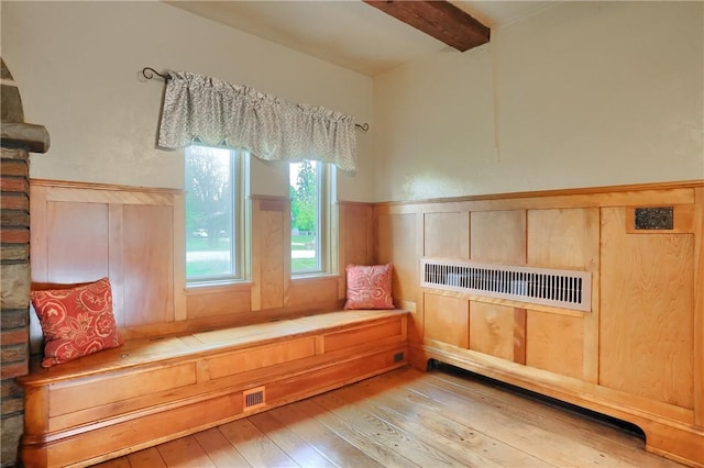 living area featuring wood-type flooring, beamed ceiling, and wainscoting