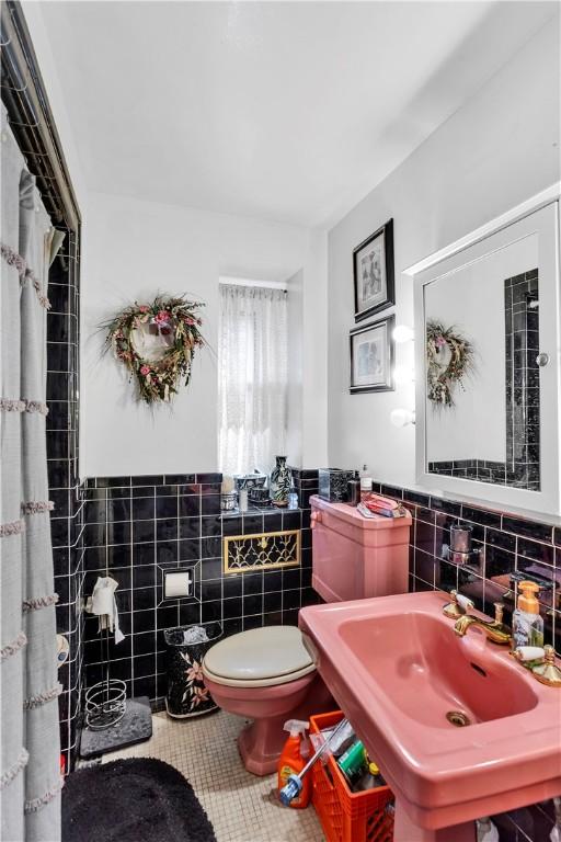 bathroom featuring tile walls, tile patterned flooring, toilet, a sink, and wainscoting