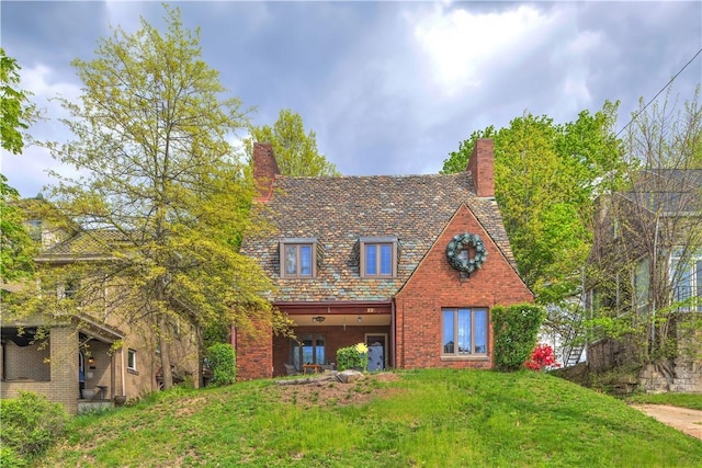 tudor house with a high end roof, a chimney, brick siding, and a front lawn