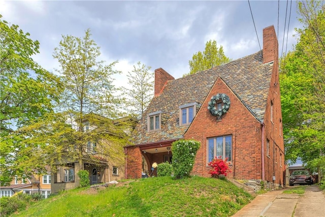 tudor house featuring a high end roof, a chimney, and brick siding