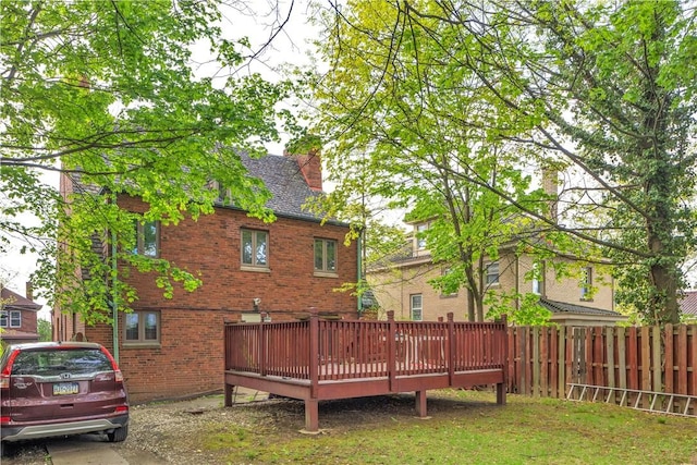 back of house featuring a chimney, brick siding, fence, and a deck