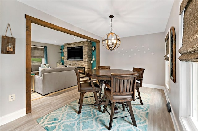 dining space with light wood-style flooring, a fireplace, a chandelier, and baseboards