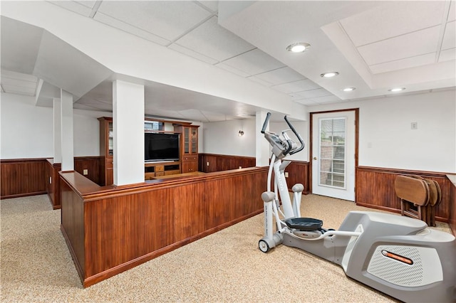exercise area with a wainscoted wall, wood walls, carpet, and a drop ceiling