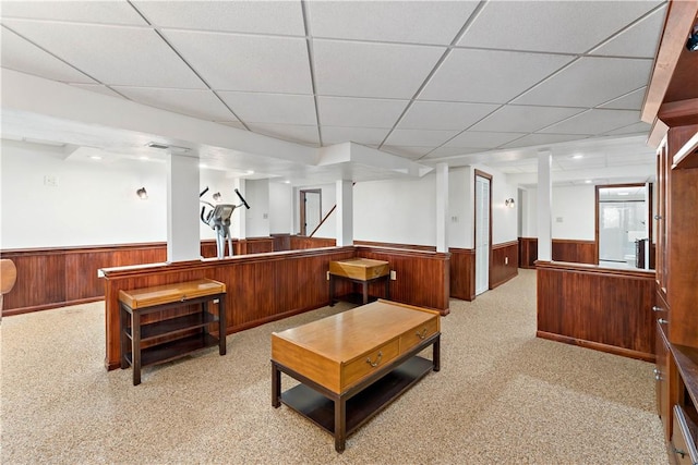 living room with wainscoting, wood walls, a paneled ceiling, and light carpet
