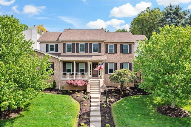 view of front of house featuring a front lawn, covered porch, stairway, and brick siding