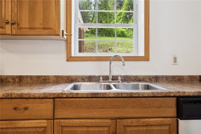 kitchen featuring a sink, dishwashing machine, and brown cabinetry