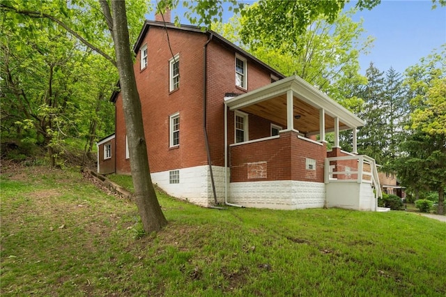 view of side of home with a yard, brick siding, ceiling fan, covered porch, and a chimney