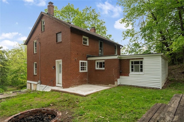 rear view of property with a chimney, brick siding, an outdoor fire pit, a patio, and a yard