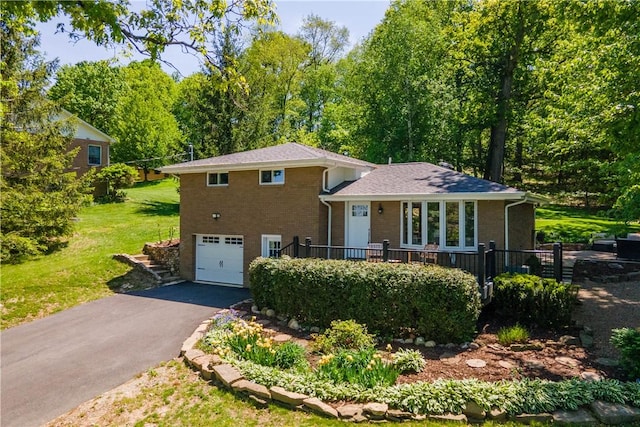 tri-level home with a garage, brick siding, driveway, and a front lawn