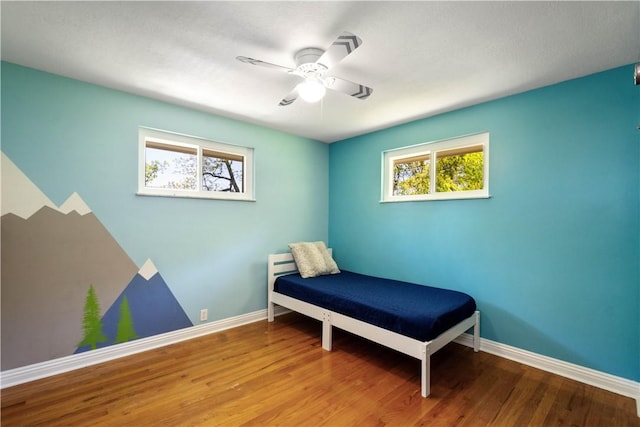 bedroom featuring multiple windows, baseboards, and wood finished floors