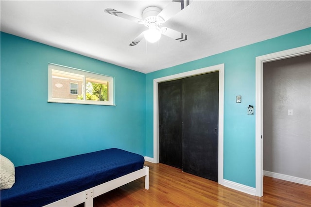 unfurnished bedroom featuring wood finished floors, baseboards, a closet, and ceiling fan