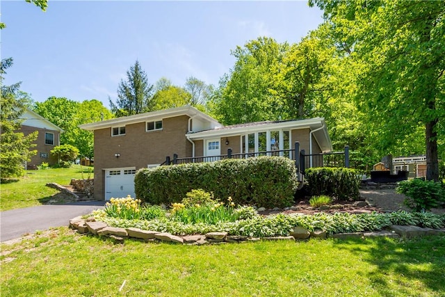 split level home with an attached garage, brick siding, asphalt driveway, a front yard, and a wooden deck